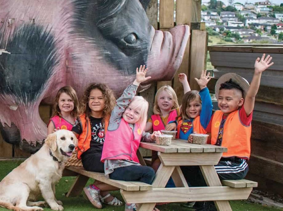 A preschool group with a dog and a piglet, waving beside the big pig